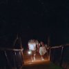 Una coppia cammina su una passerella di legno nella foresta di notte, con una lanterna.