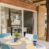 Un tavolo apparecchiato all'esterno di una casa in legno con sedie blu e grandi finestre.
