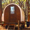 Una piccola roulotte di legno in un bosco, circondata da alberi con luci appese.