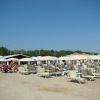 Spiaggia con lettini e ombrelloni beige, persone e cielo azzurro.