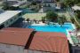 Piscina all'aperto con sedie a sdraio, edifici nelle vicinanze e alcuni ospiti che nuotano.