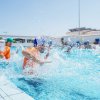 Persone giocano in piscina con schizzi d'acqua.
