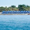 Spiaggia con fila di ombrelloni blu vicino all'acqua, alberi sullo sfondo.