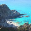 Piccola baia con spiaggia sabbiosa, rocce circostanti e acqua cristallina.