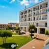 Hotel bianco con balconi, giardino curato e sfere decorative bianche.