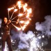 Una donna esegue un'esibizione di giocoleria con fiamme e fuochi d'artificio sullo sfondo.