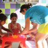 Bambini piccoli seduti a un tavolo rosso mentre fanno attività con un'animatrice.