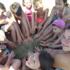 Bambini seduti in cerchio sulla sabbia con le mani a terra, sorridenti.