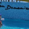 Un adulto e un bambino giocano in piscina davanti a un muro con la scritta 