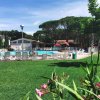 Piscina all'aperto con lettini bianchi, prato verde in primo piano e alti alberi sullo sfondo.