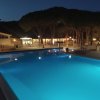Piscina illuminata di notte, con pini e edifici illuminati sullo sfondo.