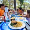 Gruppo di persone a tavola all'aperto; un panino con patatine in primo piano.