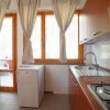 Cucina con lavello, fornelli e mini-frigo, illuminata da una porta e una finestra con tende chiare.
