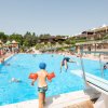 Bambini giocano in piscina, uno con i braccioli arancioni.