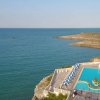 Piscina panoramica su scogliere con vista mare e ombrelloni blu.