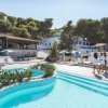 Piscina all'aperto con vegetazione, edifici bianchi e ombrelloni.