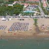 Spiaggia affollata con ombrelloni e mare, dietro ci sono strutture e piscina.
