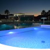 Piscina con luci blu di sera, circondata da palme e sedie a sdraio.