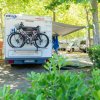 Un camper con due biciclette montate sul retro, parcheggiato in un campeggio con alberi.