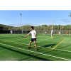 Ragazzo gioca a tennis su un campo all'aperto sotto un cielo limpido. Altri giocatori sullo sfondo.