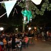 Festa serale all'aperto con tavoli, persone sedute e luci decorative.