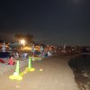Una spiaggia notturna con persone, ombrelloni colorati e un gioco gonfiabile.