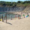 Una spiaggia di sabbia con ombrelloni colorati e persone che nuotano. Scogliere verdi sullo sfondo.