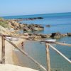 Una spiaggia rocciosa con mare calmo e ombrelloni blu.