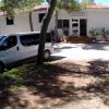 Edificio bianco con un furgone parcheggiato davanti, circondato da alberi.
