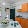 Cucina con mobili arancioni, tavolo bianco e fiori. Porta aperta verso l'esterno.