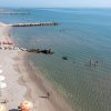 Spiaggia con mare calmo, persone in acqua, barriere frangiflutti e ombrelloni arancioni.