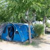 Una tenda blu piantata sotto alberi verdi in un campeggio, accanto a sedie da campeggio.