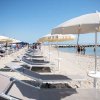 Una spiaggia sabbiosa con file di lettini e ombrelloni bianchi, persone camminano vicino al mare.