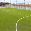 Campo di calcio in erba sintetica con linee bianche e recinzione in lontananza.