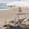 Due lettini con ombrellone bianco su una spiaggia sabbiosa, accessori sparsi.