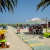 Spiaggia con palme, ombrelloni gialli e persone sedute.