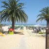 Ingresso spiaggia con palme e ombrelloni verdi.