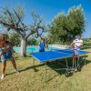 Due persone giocano a ping pong all'aperto mentre una ragazza osserva.