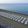 Spiaggia con file di ombrelloni bianchi, mare calmo e un ombrellone rosso in mezzo.