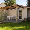 Un bungalow con veranda, tavolo bianco e sedie, circondato da prato verde e alberi.