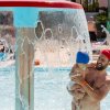 Uomo con bambino sotto una fontana a cascata in una piscina.