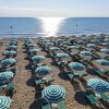 Spiaggia con fila di ombrelloni a righe verde e bianco e lettini di fronte al mare.