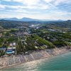 Vista aerea di una spiaggia affollata con ombrelloni e resort circondati da colline e vegetazione.