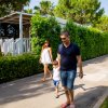 Due adulti e un bambino camminano su un vialetto, circondati da alberi e siepi.