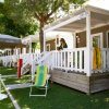 Veranda di bungalow con persona e lettino verde su prato erboso.
