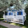 Casetta bianca con persiane blu e veranda, circondata da alberi.