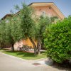 Esterno di edificio rosa con balconi, biciclette parcheggiate e alberi verdi intorno.