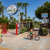 Cancello rosso con cartello Don Antonio, palme e una persona in bicicletta.