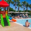 Piscina con scivolo colorato e persone rilassate sotto ombrelloni.