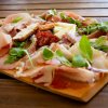 Un tagliere di legno con affettati, formaggi e rucola su un tavolo di legno.